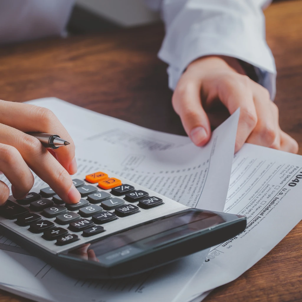 Imagem de uma mão realizando cálculos em uma máquina calculadora em cima de uma mesa ilustrando o texto Consultoria Jurídica Tributária